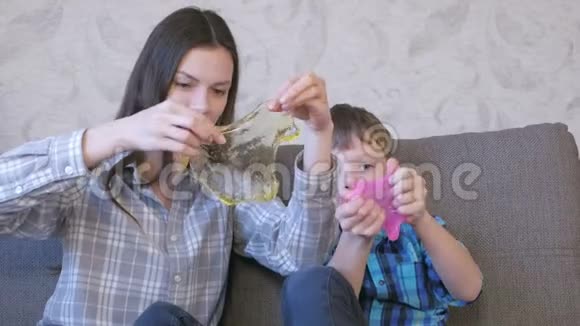 快乐的妈妈和儿子坐在沙发上玩黏液伸展的黏液透过黏液视频的预览图