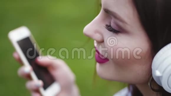 有魅力的年轻女性淡妆艳抹红唇在智能手机上听音乐有感情地唱歌视频的预览图