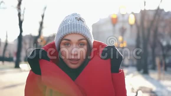 在一个阳光明媚的冬日穿着红色夹克的漂亮女人站在满是雪的街道上视频的预览图