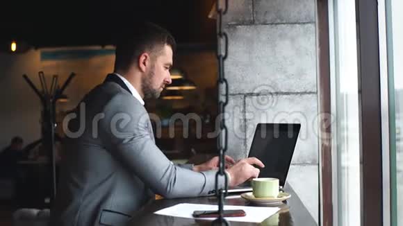 一个留着胡子的男人企业家坐在咖啡馆里做远程工作时拿着笔记本电脑视频的预览图