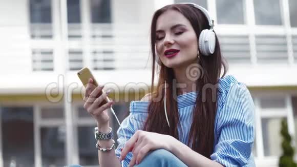 漂亮时髦的女人用耳机听手机里的音乐闭上眼睛边唱边做手势视频的预览图