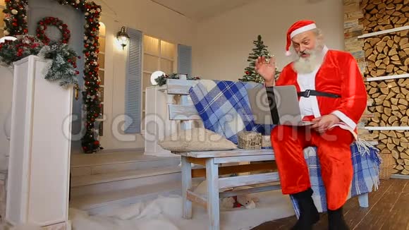 圣诞老人在电脑上玩电视游戏聊天坐在装饰庭院的长椅上度假视频的预览图