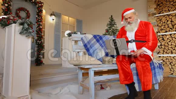 圣诞老人在电视上讲话圣诞精灵在笔记本电脑上坐在装饰庭院的长凳上度假视频的预览图