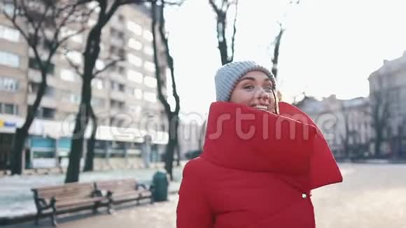 在一个阳光明媚的冬日穿着红色夹克的漂亮女人站在满是雪的街道上视频的预览图