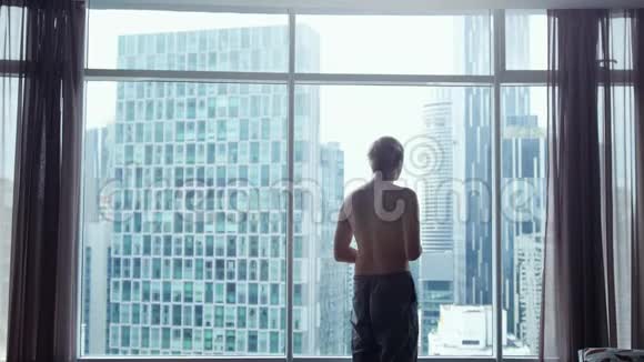 从穿短裤的年轻人身后眺望城市美景从窗户可以看到天际线和标志性建筑视频的预览图
