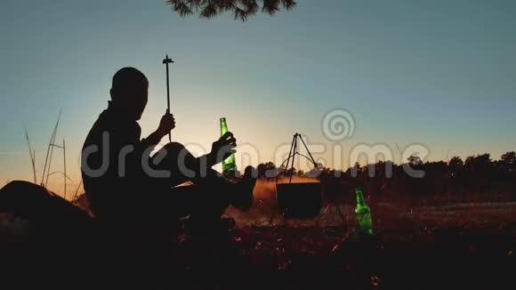 两名游客的舞蹈正坐在篝火晚会上在大自然中露营剪影阳光日落两个男人剪影视频的预览图