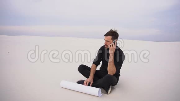 慢动作建设者男性在智能手机上与朋友坐在沙滩上交谈视频的预览图