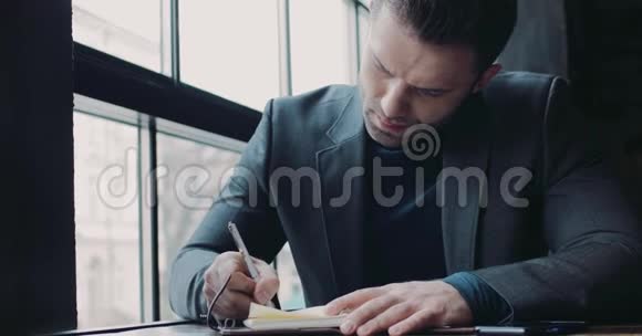 一个欧洲年轻人在窗户旁的咖啡馆做笔记正式穿着商业生活成功的生活方式作为一个视频的预览图