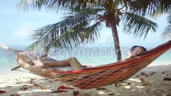 年轻人在热带海滩的吊床上放松在棕榈树旁边的吊床上睡觉的人慢动作1920x1080视频的预览图