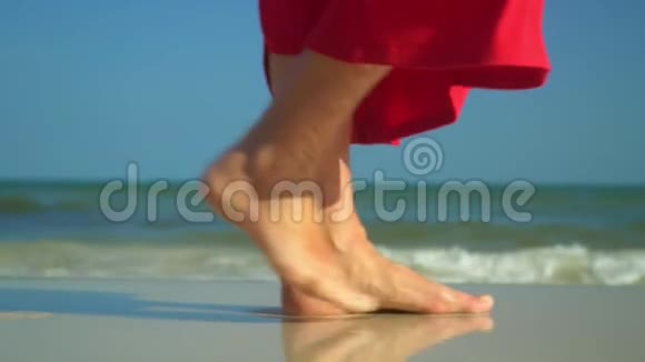 女人双腿合拢背景上的海洋那个穿红色衣服的女人在海滩上散步视频的预览图