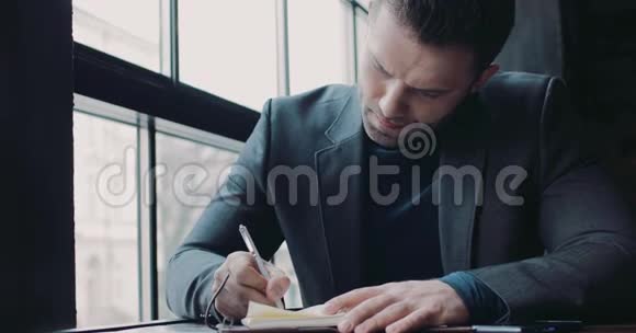 一个穿着正式服装的留胡子的年轻人在一家咖啡馆A上写下报纸上的想法做老板成功视频的预览图