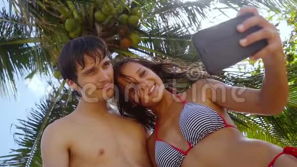 浪漫的幸福的情侣在阳光下在户外的棕榈树下在手机上自拍在阳光下和视频的预览图