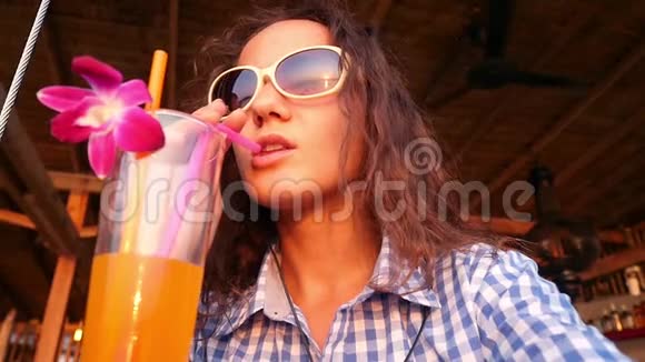 年轻漂亮的女士戴着太阳镜享受着装饰着鲜花的热带鸡尾酒并在视频的预览图