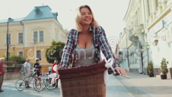 迷人的金发美女短发穿着休闲装骑着老式自行车在老市中心笑着视频的预览图