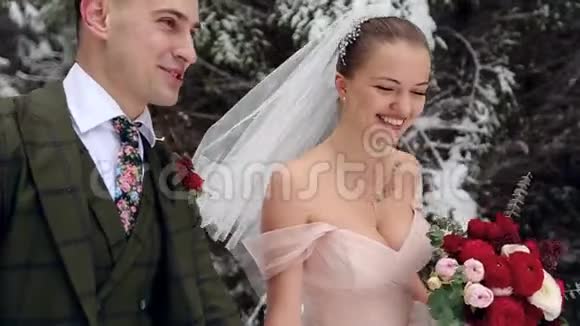 年轻的新婚夫妇走着微笑着说话在下雪的森林里牵手冬季婚礼视频的预览图