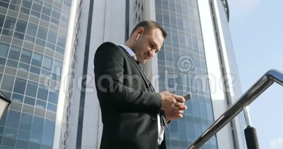 在城市智能手机上使用应用程序短信英俊的年轻商人用智能手机微笑快乐城市男性视频的预览图