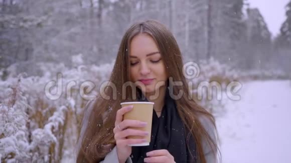 美丽的年轻女子带着一次性咖啡杯正在户外的冬季公园里喝茶或咖啡慢动作视频的预览图