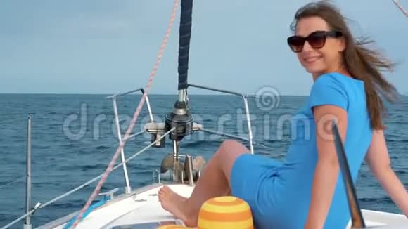 穿着黄色帽子和蓝色连衣裙的女人在海洋的夏天在游艇上挥舞着头发和微笑慢动作视频的预览图