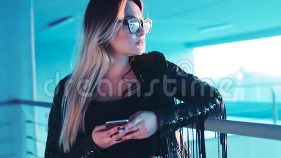 漂亮的金发女人戴着眼镜和时髦的皮夹克环顾四周发短信社会网络现代视频的预览图