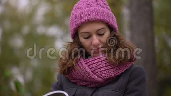 一个年轻漂亮的女人在秋天在公园里读日记秋季公园阅读放松视频的预览图