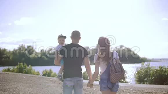 年轻夫妇带着一个孩子手牵着手走向河边视频的预览图