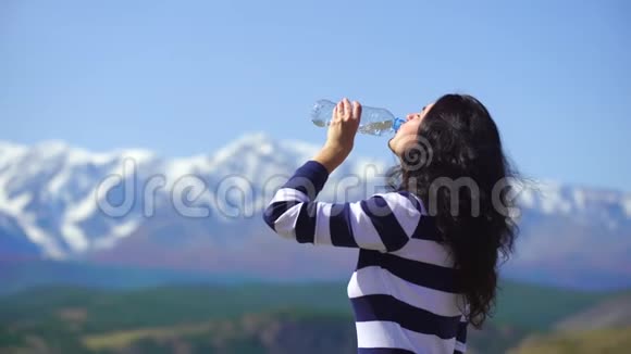 美丽的年轻女子旅行者在美丽的山脉背景上喝水女人在山顶放松视频的预览图