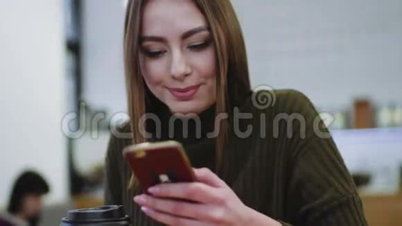 穿着时髦毛衣的年轻女子坐在咖啡馆里喝着咖啡发短信开心地笑着视频的预览图