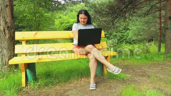 在公园里坐长凳的年轻女人用笔记本电脑工作视频的预览图