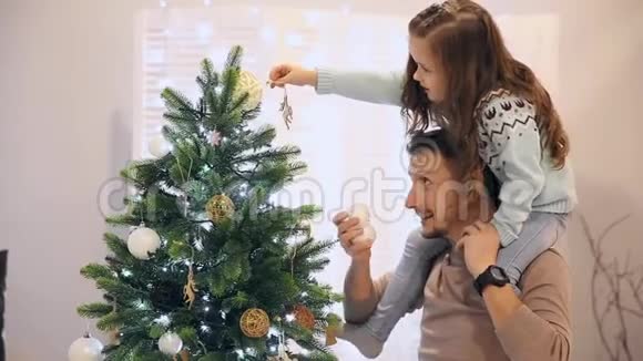 女孩坐在爸爸的脖子上他们装饰圣诞树视频的预览图