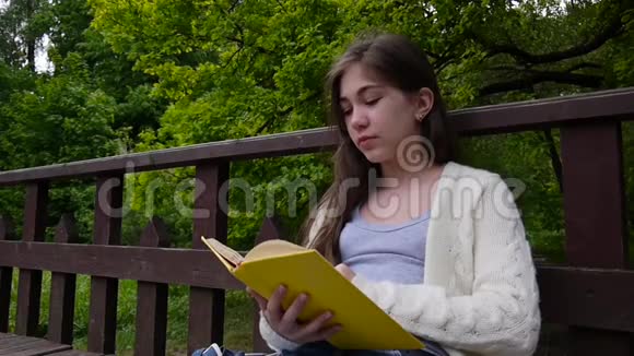 一幅严肃的少女阅读书和翻页的肖像春天倚在森林的长凳上视频的预览图
