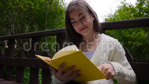 一幅严肃的少女阅读书和翻页的肖像春天倚在森林的长凳上视频的预览图
