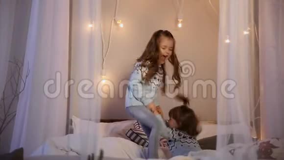 两个姐妹在圣诞节穿着毛衣在床上跳跃玩得很开心笑着拥抱视频的预览图