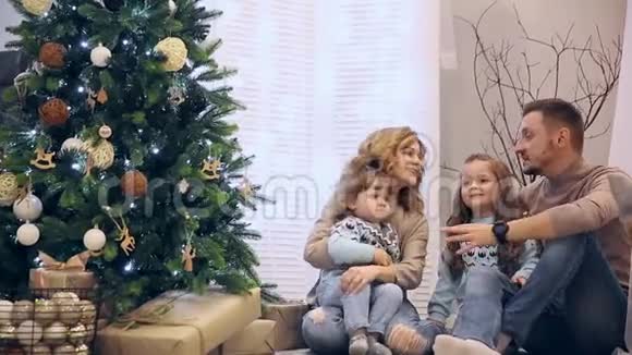 圣诞快乐一家人穿着毛衣爸爸妈妈和两个女儿坐在树下笑着互相买东西视频的预览图