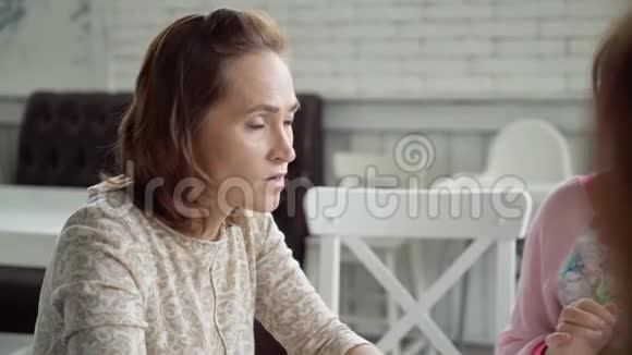 一个漂亮的女人向坐在餐桌旁咖啡馆的同事解释在咖啡馆吃午饭布鲁内特的同事视频的预览图