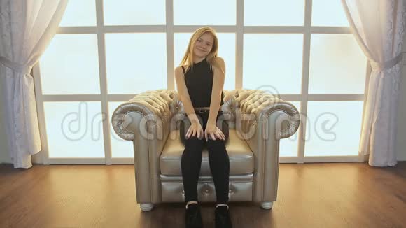 一个十几岁的女孩坐在照相馆大厅里柔软的扶手椅上跳舞跳得很有趣在一个视频的预览图