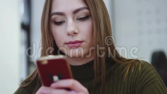 一位年轻女性坐在一家舒适的咖啡馆里用手机近距离观看得到信息开心地微笑着视频的预览图