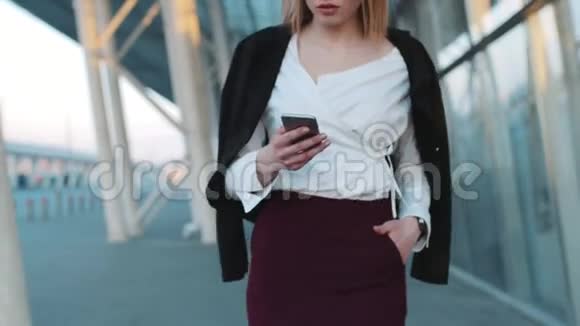 美丽的金发欧洲女孩用她的手机穿过机场候机楼看着镜头视频的预览图