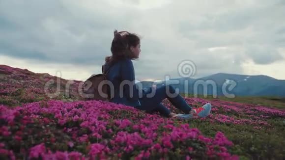 一位年轻貌美的女士背着背包坐在山顶上身穿盛开的薰衣草视频的预览图
