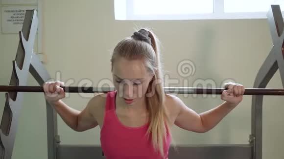一个穿着粉红色背心的金发女郎做一个运动她的肩膀上有一个杠铃视频的预览图