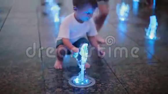 在炎热的夏天可爱的小男孩在喷泉边玩彩色喷水跑向一群孩子视频的预览图