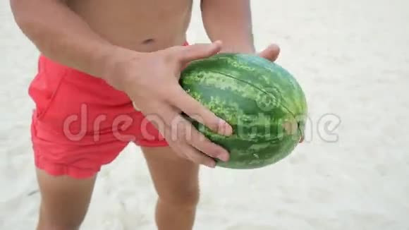 年轻英俊的素食主义者在海滩上用强壮的双手把西瓜分成两个半泰国高清慢速运动视频的预览图