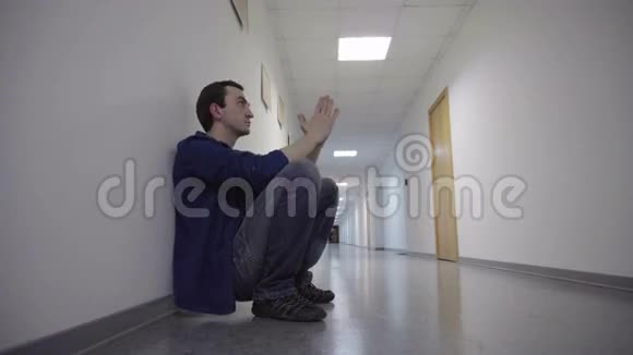 男人蹲在长长的白色走廊里靠在墙上祈祷希望和等待视频的预览图