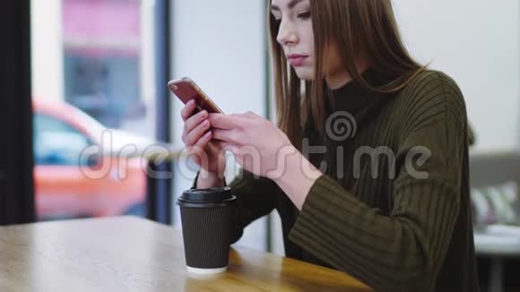 漂亮的欧洲女孩穿着时尚的休闲服独自坐在窗边使用她的智能手机现代生活方式视频的预览图