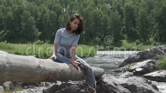 坐在水上树干上的迷人女孩视频的预览图