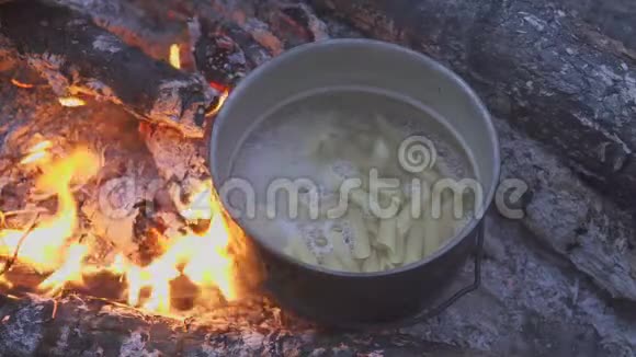 在晚林的篝火上用大锅煮意大利面厨师用勺子搅动食物特写视频的预览图