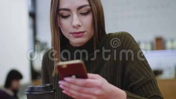 漂亮的黑发女孩穿着时髦的休闲装独自坐在一家咖啡馆的窗户旁用她的智能手机得到了视频的预览图