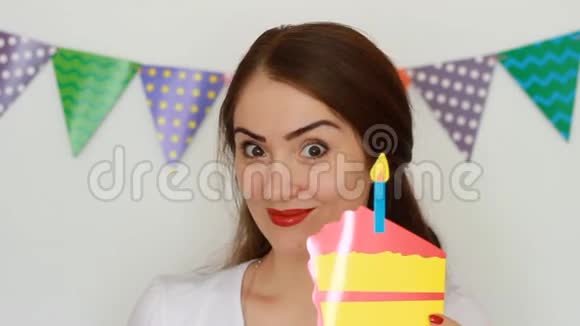 那个有趣的女孩微笑着手里拿着蛋糕吹出一支纸烛年轻快乐女人特写的肖像视频的预览图