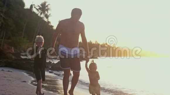 快乐的父亲牵着孩子们手在美丽的夕阳下在热带海滩上散步旅游度假概念慢慢慢慢视频的预览图