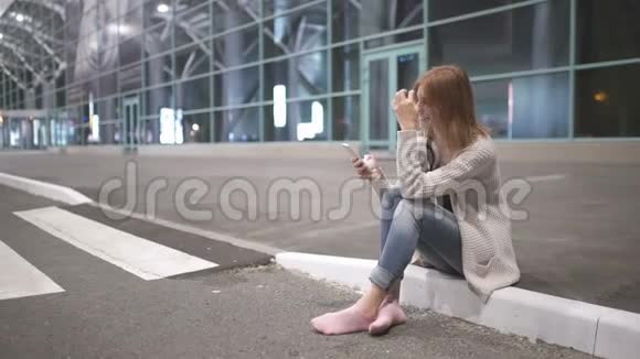 美丽的红发女人晚上在城市街道上使用智能手机技术视频的预览图