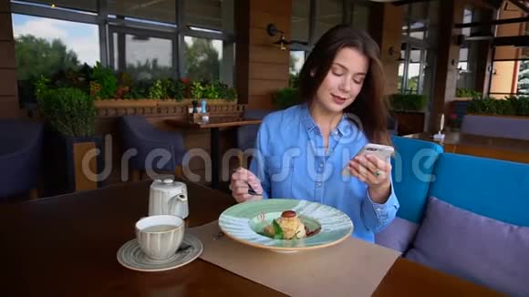 漂亮的女人坐在咖啡馆里用智能手机聊天慢慢地吃甜点视频的预览图